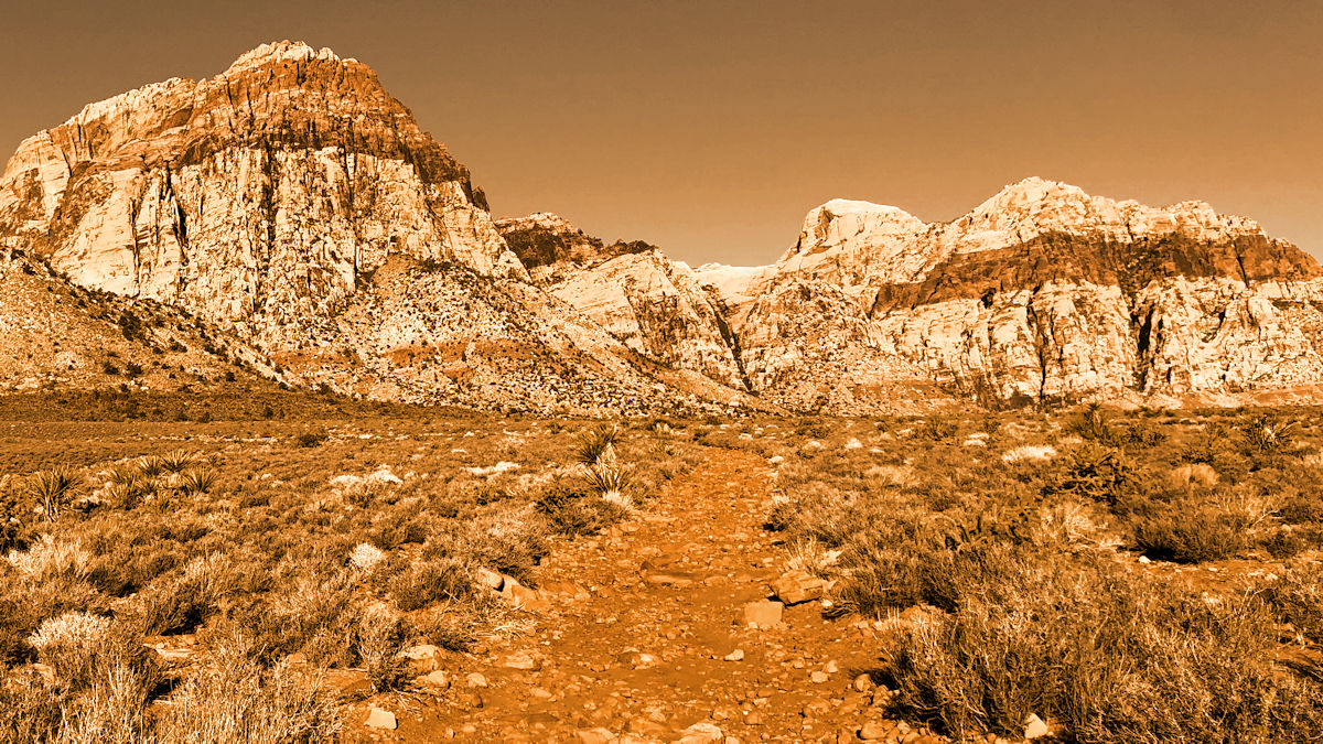 Desert trail leading toward rugged red rock mountains under a burnt orange sky